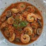 Authentic Seafood Fra Diavolo with shrimp, clams, and a spicy tomato sauce, garnished with fresh herbs in a white ceramic plate.