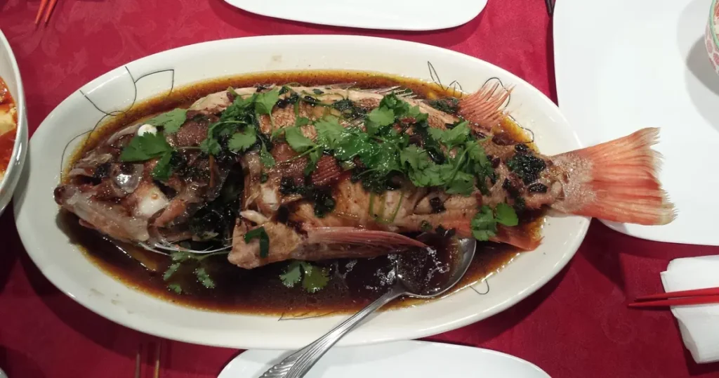 Whole grilled tilapia with golden crispy skin served on a wooden platter with lemon slices and fresh herbs.