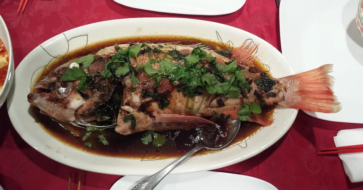 Whole grilled tilapia with golden crispy skin served on a wooden platter with lemon slices and fresh herbs.